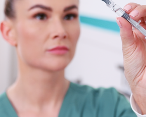 Medizinische Fachangestellte schaut Impfstoff in einer Spritze an